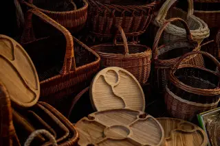 Ilustrasi: Kumpulan keranjang anyaman rotan dan piring kayu kerajinan tangan tertata rapat.