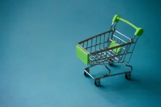 Ilustrasi: Miniatur kereta belanja beraksen hijau di atas latar belakang biru polos.