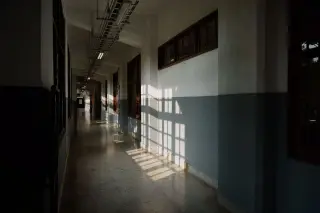 Ilustrasi: Lorong gedung yang sepi dengan bayangan teralis jendela tersorot cahaya matahari di dinding.
