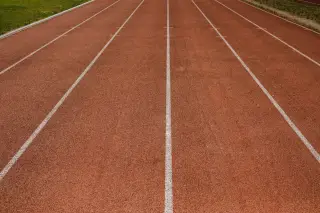 Ilustrasi: Lintasan lari atletik berwarna merah bata dengan garis putih pembatas lajur.