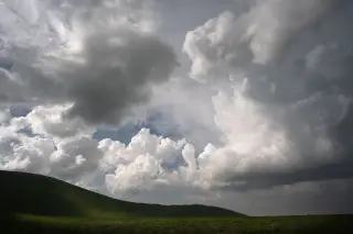 Ilustrasi: Pemandangan perbukitan hijau dengan hamparan langit berawan tebal mendung.