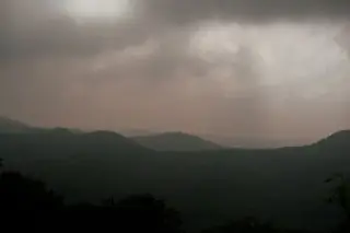 Ilustrasi: Pemandangan perbukitan hijau di bawah langit kelabu berawan mendung.