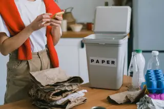 Ilustrasi: Seseorang memegang ponsel di dekat tempat sampah pilah kertas dan tumpukan daur ulang.