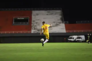 Ilustrasi: Pemain sepak bola berseragam kuning menendang bola di lapangan hijau pada malam hari.