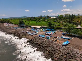 Ilustrasi: Pemandangan udara perahu-perahu nelayan bersandar di pesisir berbatu dekat pepohonan hijau.