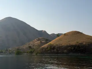 Pemandangan laut tenang dengan bukit-bukit kering dan beberapa bangunan kecil di tepi pantai. Kelor, Rabu (23/9/2026).