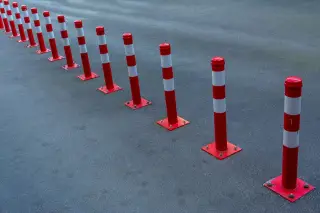 Ilustrasi: Deretan tiang pembatas jalan berwarna merah putih berbaris di atas aspal.