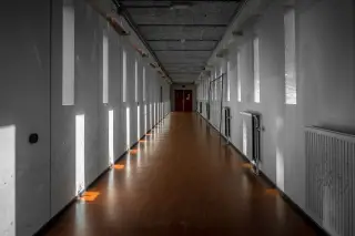 Ilustrasi: Lorong panjang dan sunyi di dalam gedung dengan cahaya matahari masuk dari celah jendela vertikal.