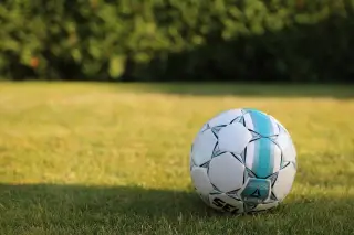 Ilustrasi: Sebuah bola sepak putih bermotif biru tergeletak di atas rumput hijau.
