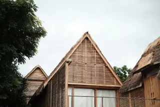 Ilustrasi: Deretan bangunan kayu beratap jerami dengan kisi-kisi bambu di bawah langit berawan.