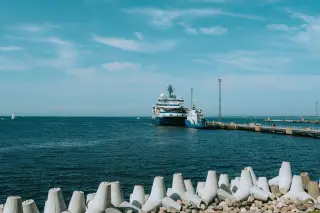 Ilustrasi: Kapal besar bersandar di dermaga laut dengan pemecah gelombang beton di latar depan.