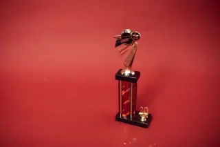Ilustrasi: Sebuah piala berwarna emas dan hitam berdiri di atas latar belakang merah polos.