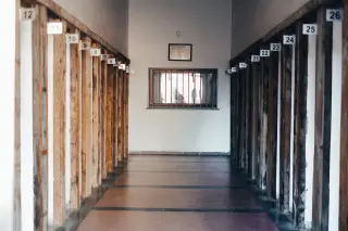 Ilustrasi: Lorong kosong dengan pilar-pilar bernomor dan jendela berterali di ujungnya.
