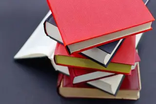 Ilustrasi: Tumpukan beberapa buku tebal bersampul merah dan hitam di atas latar gelap.