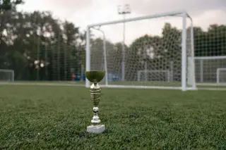Ilustrasi: Sebuah piala emas kecil berdiri di atas rumput lapangan sepak bola dengan latar gawang.