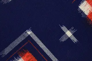 Ilustrasi: Detail jarak dekat kain tenun berwarna biru tua dengan motif geometris putih dan oranye.