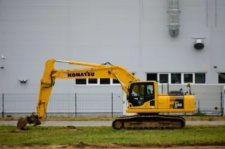 Ilustrasi: Sebuah ekskavator kuning terparkir di depan dinding gedung modern.