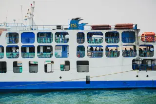 Ilustrasi: Tampak samping kapal feri penumpang berwarna putih biru di atas air laut.
