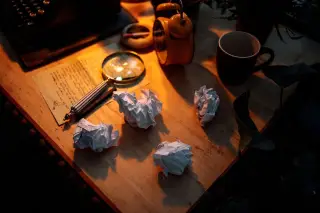 Ilustrasi: Kaca pembesar, kertas kusut, dan jam weker di atas meja kayu dengan pencahayaan hangat.