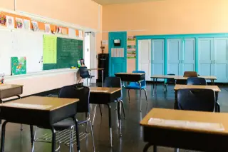 Ilustrasi: Ruang kelas kosong dengan jajaran meja dan kursi serta papan tulis di dinding.