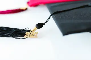 Ilustrasi: Toga wisuda dengan rumbai dan gantungan angka tahun 2021 di atas permukaan putih.