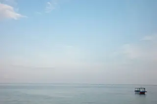 Ilustrasi: Sebuah perahu kecil terapung di laut tenang di bawah langit biru cerah.