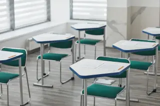 Ilustrasi: Deretan meja dan kursi kosong di dalam ruang kelas dengan lembar kertas di atas meja.