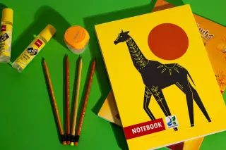 Ilustrasi: Buku tulis bersampul kuning, pensil kayu, rautan, dan lem di atas latar hijau.