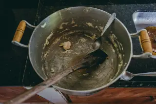 Ilustrasi: Panci aluminium besar berisi sisa adonan dan sendok di atas meja dapur.