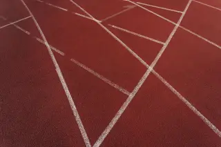 Ilustrasi: Pemandangan jarak dekat lintasan lari atletik berwarna merah dengan garis-garis putih.