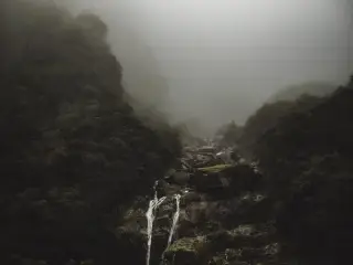 Ilustrasi: Air terjun kecil mengalir di lereng bukit berbatu yang diselimuti kabut tebal.
