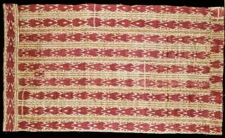Ilustrasi: Sebidang kain tenun ikat tradisional dengan motif geometris berwarna merah dan krem berlatar hitam.