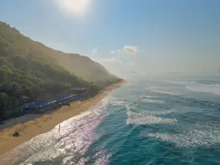 Ilustrasi: Pemandangan pantai berpasir dan laut berombak di samping tebing hijau dari udara.