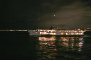 Ilustrasi: Sebuah kapal penumpang dengan lampu menyala berlayar di laut pada malam hari.