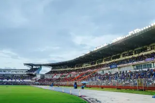 Ilustrasi: Pemandangan tribun stadion olahraga yang dipadati penonton di samping lapangan rumput.