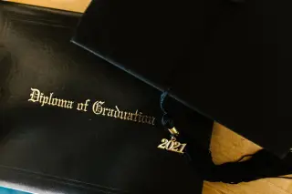 Ilustrasi: Topi toga wisuda dengan gantungan tahun 2021 di atas map ijazah bertuliskan Diploma of Graduation.