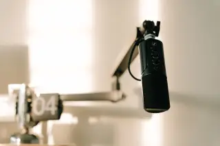 Ilustrasi: Mikrofon profesional hitam terpasang pada lengan penyangga di dalam studio berpenerangan hangat.