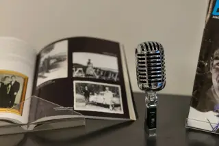 Ilustrasi: Mikrofon antik berbahan krom berdiri di atas meja dekat buku album terbuka.