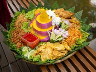 Ilustrasi: Sajian tumpeng nasi kuning lengkap dengan lauk-pauk beralaskan daun pisang di atas tampah bambu.