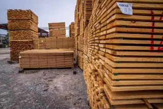 Ilustrasi: Tumpukan papan kayu tersusun rapi di area penyimpanan terbuka.