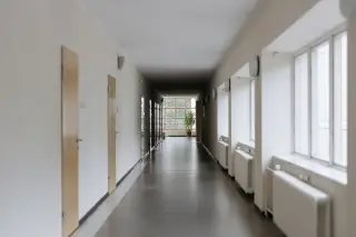 Ilustrasi: Lorong bangunan kosong bernuansa putih dengan jajaran pintu kayu dan jendela kaca.