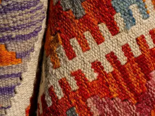 Ilustrasi: Detail jarak dekat dari kain tenun bermotif tradisional dengan benang tebal warna-warni.