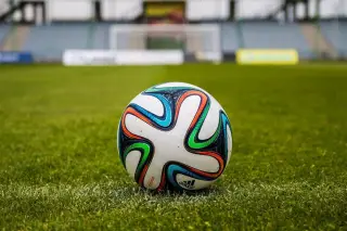 Ilustrasi: Sebuah bola sepak bermotif warna-warni terletak di atas rumput lapangan hijau.