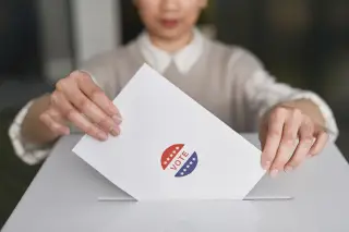 Ilustrasi: Seseorang memasukkan amplop bertuliskan vote ke dalam kotak suara putih.