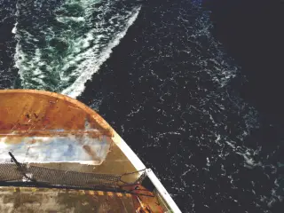 Ilustrasi: Sudut kapal feri membelah air laut yang berbusa dilihat dari atas.