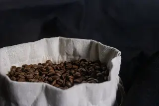 Ilustrasi: Biji kopi sangrai di dalam kantong kain kecil dengan latar belakang gelap.