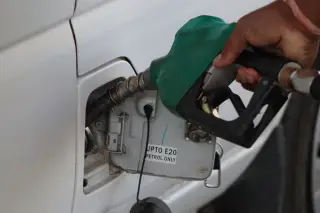 Ilustrasi: Tangan seseorang memegang nozel bahan bakar hijau yang dimasukkan ke tangki mobil putih.
