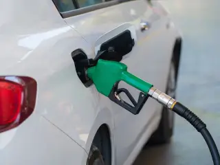 Ilustrasi: Nozel pompa bahan bakar berwarna hijau terpasang pada tangki mobil putih.