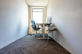 Ilustrasi: Ruang kantor sempit dengan meja kerja, kursi, dan komputer di dekat jendela.