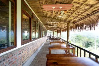 Ilustrasi: Balkon kafe beratap jerami dengan deretan meja kayu yang menghadap ke pemandangan alam.